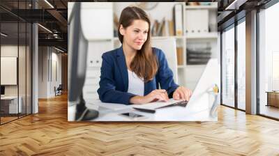 Portrait of successful busy female entrepreneur sitting at office desk with papers and laptop Wall mural