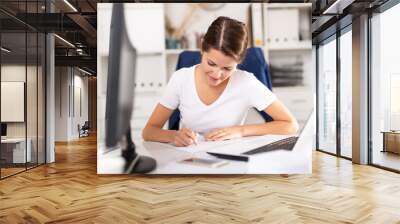 Portrait of successful busy female entrepreneur sitting at office desk with papers and laptop Wall mural