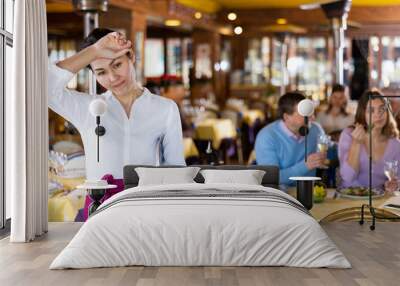 Portrait of tired Asian woman waitress with tray standing in restaurant. Wall mural