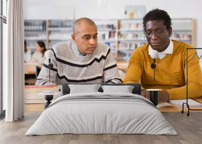 Portrait of two adult men engaged in research, looking together for information in books in library Wall mural