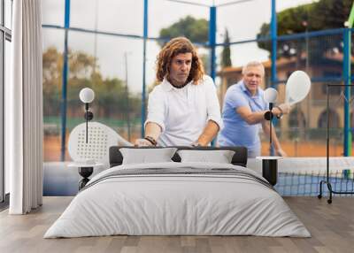 Portrait of two mature male tennis partners enjoying popular sport padel game with rackets outdoors Wall mural