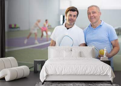 Portrait of two men pickleball players with rackets and a ball standing on an indoor court Wall mural