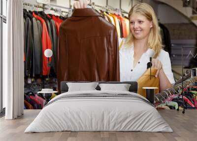 Positive girl looking for new leather jacket during shopping in retail shop Wall mural