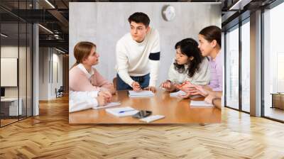 Positive motivated young guy, student team leader holding meeting with group, explaining details of new study project Wall mural