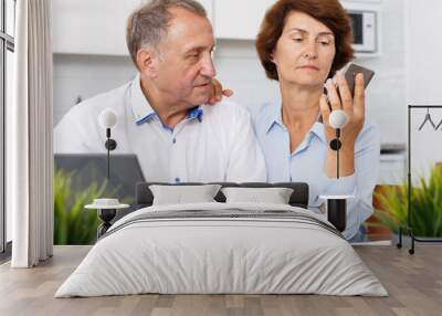 Positive senior man and woman with phone at laptop in home interior Wall mural