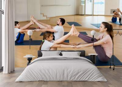 Positive sporty teen girl practicing partner yoga in pair with mother during training with family in fitness center.. Wall mural