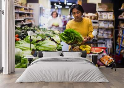 Positive woman choosing food products on shelves in grocery shop Wall mural