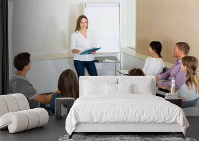 Positive young female business coach communicating with adult auditorium during training in office Wall mural