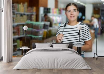 Positive young woman strolling through local grocery store, curiously looking at various food products on shelves.. Wall mural