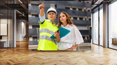 Professional builder man talking with woman client while standing at construction site, pointing to something Wall mural