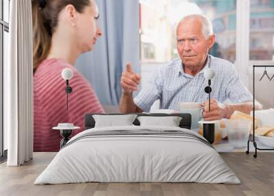 Senior man talking with young sad daughter and  pointing to mistakes Wall mural