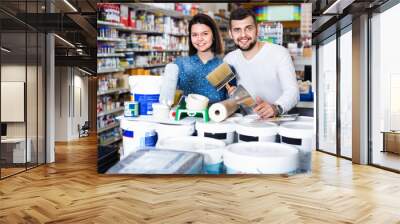 Smiling cheerful couple purchasing tools for house improvements in paint supplies store Wall mural