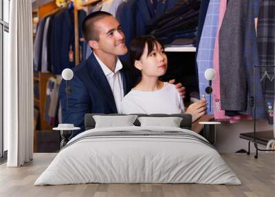 Smiling couple examining various suits in mens cloths store Wall mural