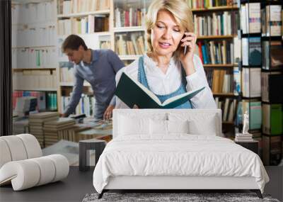 Smiling mature woman customer looking at book Wall mural