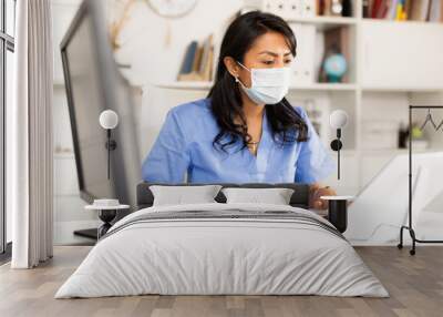 Smiling peruvian female therapist working with case histories on laptop in modern medical office Wall mural