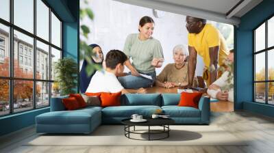 Smiling young girl participating in volunteer work discussing goals and objectives of project or event with group of associates, men and women of different ages and nationalities gathered around table Wall mural