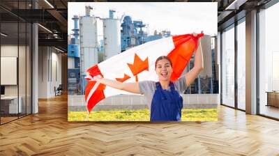 Smiling young woman in uniform posing with Canada flag near factory Wall mural