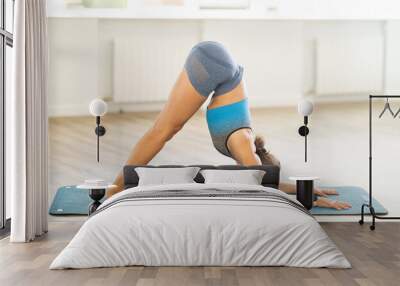 Sportive young girl practicing downward facing dog pose of yoga on blue mat in light room Wall mural