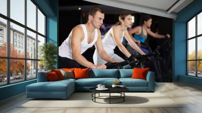 Sportive young man doing spin bike exercises in well-equipped gym during training session Wall mural