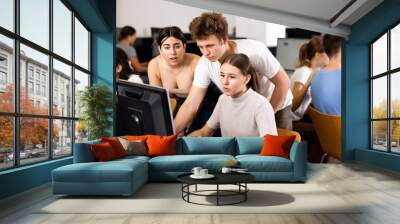 Teenager boy and girls studying in computer class, working on task solution together and using computer. Wall mural