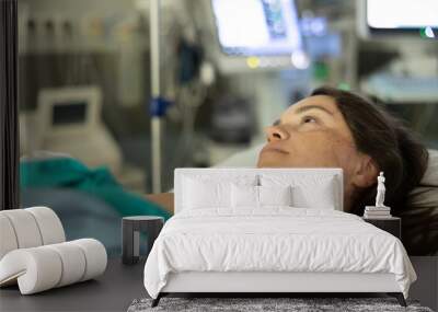 Tired calm woman resting after surgical intervention in hospital bed in surgery, connected to intravenous line, against blurred background of medical devices Wall mural