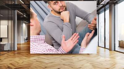 Troubled man having serious talk with his friend on sofa at home Wall mural