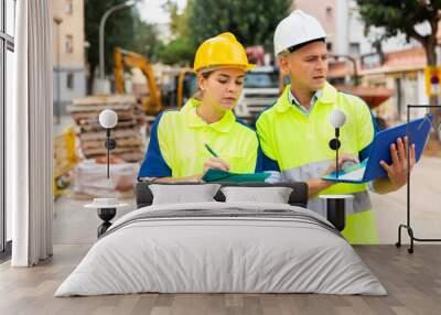 Two civil engineers with laptop and documents checking work process in construction site outdoors Wall mural