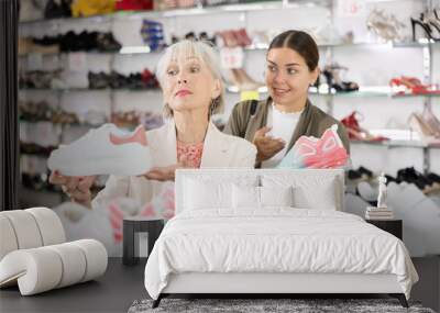 Two positive women of different ages choose new sneakers together in a fashion store Wall mural