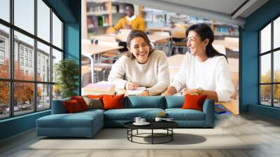 Two young adult women gaining new skills at public library, reading books and making notes Wall mural