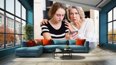 Upset mature mother with adult daughter using smartphone in kitchen interior Wall mural