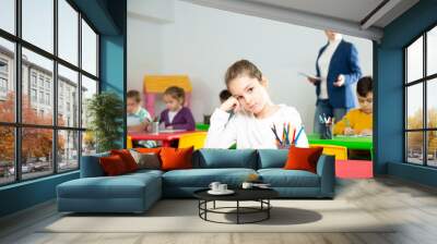 Upset schoolgirl sitting at a desk in classroom elementary school Wall mural