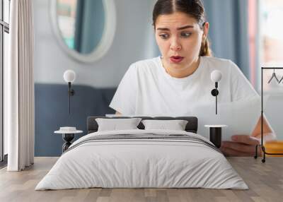 Upset woman with financial documents sitting at the table at home Wall mural