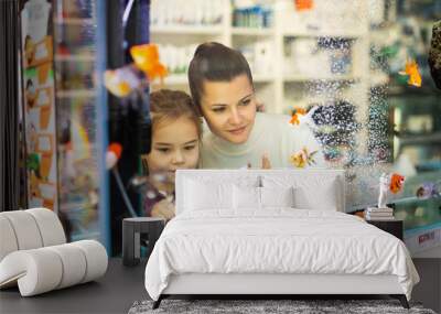 View through aquarium glass of young woman with little girl looking at colorful tropical fish in pet shop Wall mural