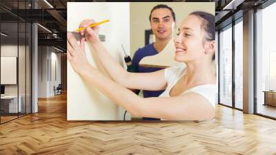 Wife with husband hanging bookshelf at home Wall mural