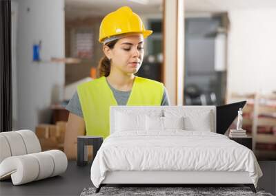 Woman construction worker standing and using laptop in building site. Wall mural