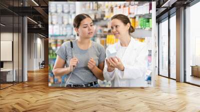 Woman listens to pharmacist s speech about products for daily facial skin care and examines packaging of cream Wall mural