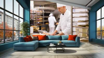 Working at bakery, male baker kneading dough and shaping baguettes on steel countertop in industrial kitchen Wall mural