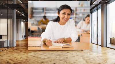 Young adult woman working with books, finding information at library Wall mural