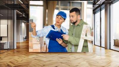 Young bearded interior designer standing with papers in hands in apartment during renovation, talking to female professional building contractor Wall mural