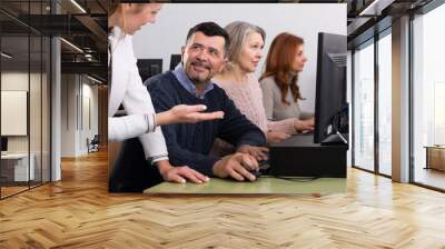 Young female teacher explaining computer skills to mature man in university class.. Wall mural