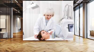 Young female visitor receiving hardware electric lifting massage with help of old female beautician in spa salon indoors Wall mural