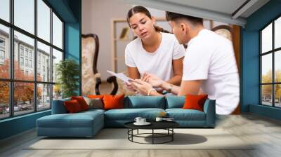 Young focused married couple attentively studying important documents, sitting at a desk in an apartment Wall mural