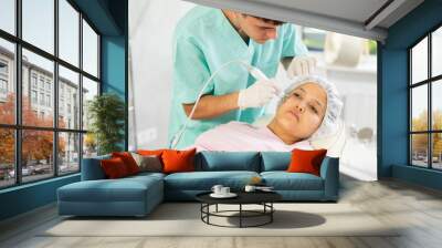 Young male cosmetologist performs hardware facial microcurrent procedure to young female patient Wall mural