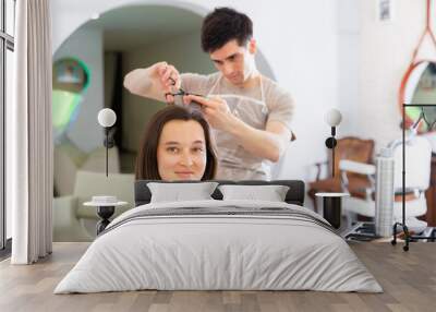 Young man stylist working in hairdressing salon doing haircut and hair styling for female client Wall mural