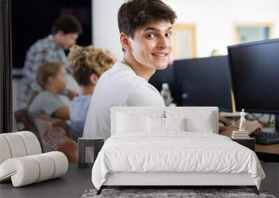 Young man working on computer together with other underage attendees of IT courses Wall mural