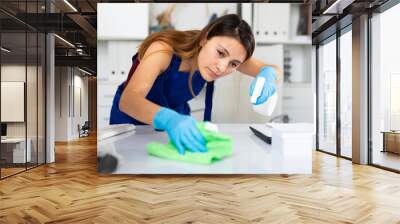 Young mexican woman wearing uniform cleaning table with spray at company office Wall mural