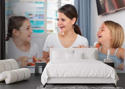 Young mother and two daughters eating healthy food with vegetables in living room Wall mural