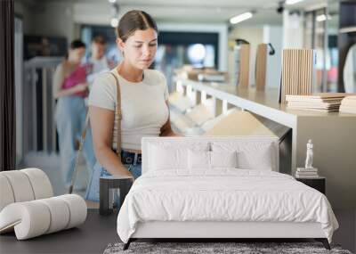 Young woman buyer chooses sample of laminate flooring in hardware store Wall mural