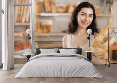 Young woman buyer chooses tasty fresh baguettes in bakery Wall mural