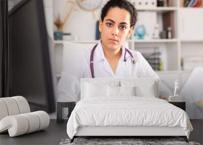 Young woman doctor assistant working in medical office using laptop computer and writing prescription Wall mural